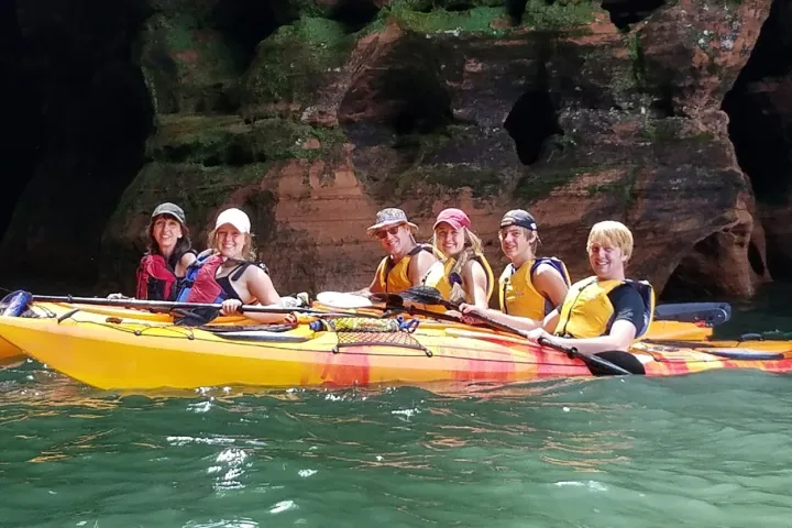 A group of people smiling in life vests while in kayaks at Aspostle Island