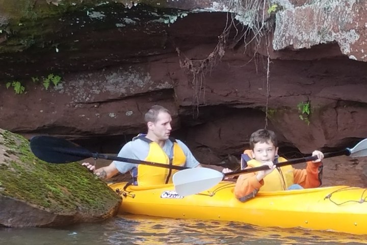 A man and a boy kayaking under a rock overhang
