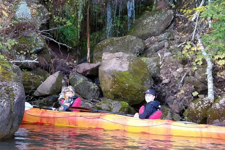 Two boys in a tandem kayak near a waterfall