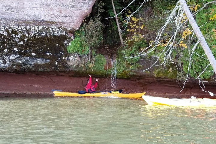 A man kayaking under a waterfall under red cliff caves
